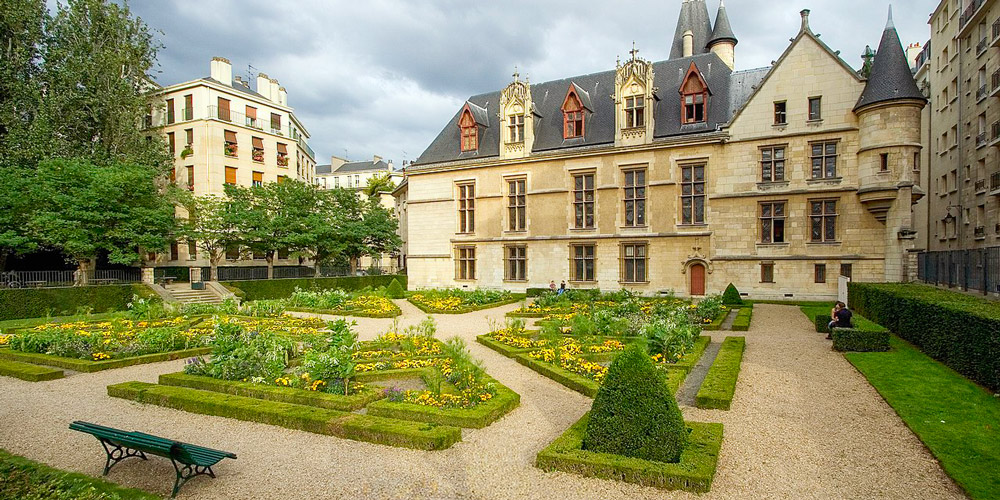 The garden of Hotel de Sens with paths, benvhes, and yellow flowering plants