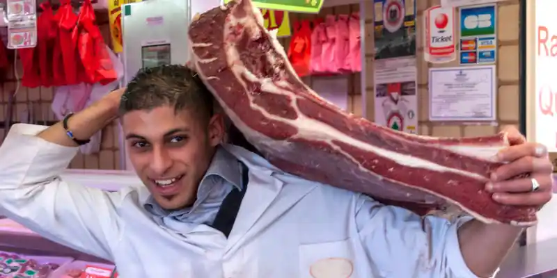 Food vendor carrying a large piece of meet at the Aligre boucherie