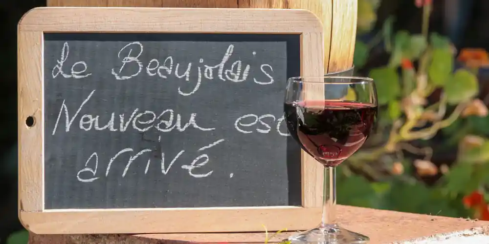 Glass of Beaujolais Nouveau beside a chalkboard announcing its arrival