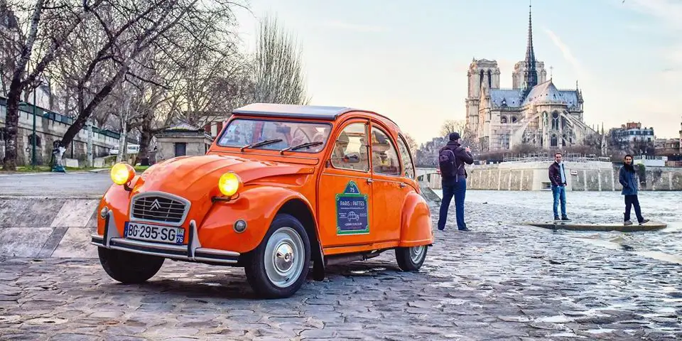 An orange 2CV on the banks of the Seine with Notre Dame in view