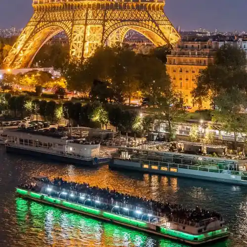 Seine River dinner cruise boat passing beneath the Eiffel Tower at night