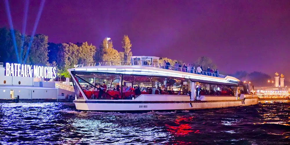 A Bateaux Parisiens dinner boat cruises on the Seine beneath Notre Dame at twilight