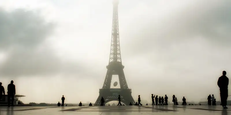 Visitors gather beneath the Eiffel Tower on a misty morning