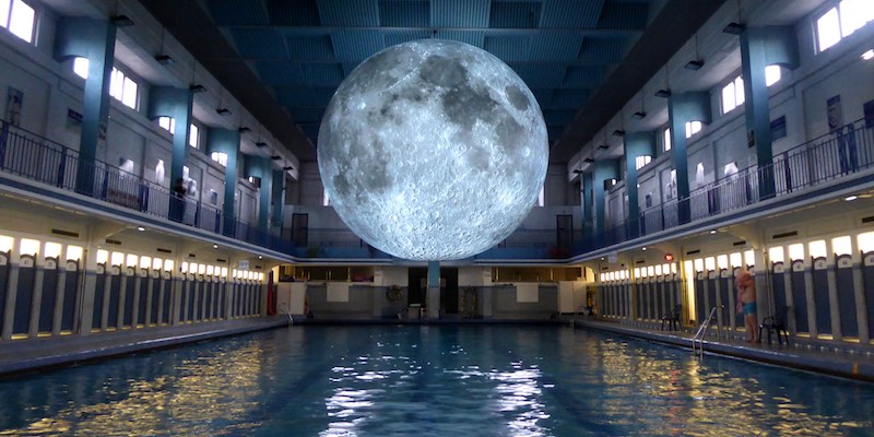 A large moon floats above a swimming pool, an art installation during Festival Paris l'Ete