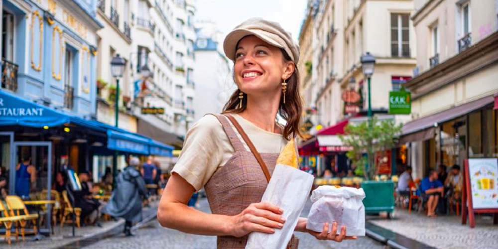 A smiling owman with a baguette and pastries on the streets of Paris