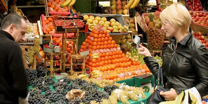 A Parisienne shopping at the Market on Rue Poncelet,  apile of oranges beside her.