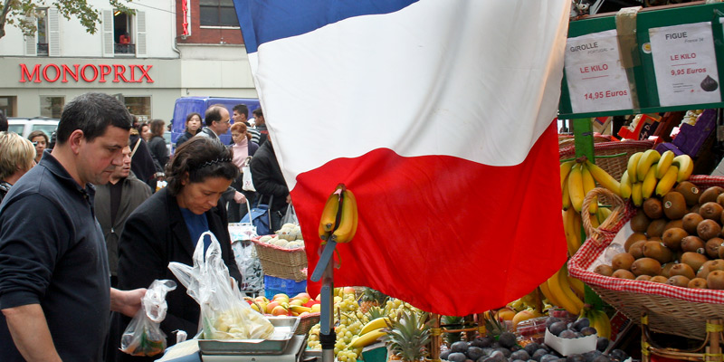 Beneath a French flag, Parisians shop for produce on Rue Poncelet, photo by Mark Craft