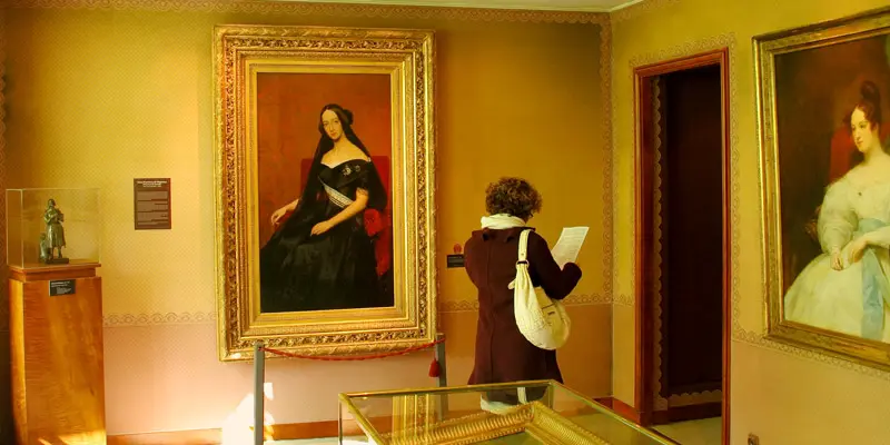 At Musee de la Vie Romantique a visitor reads an information sheet while portraits seems to gaze down on her