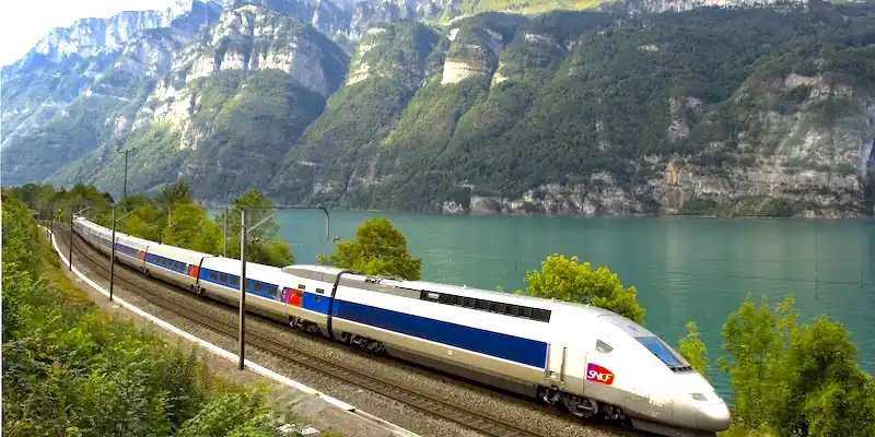 A high-speed TGV trains speeds along a river in a mountain setting
