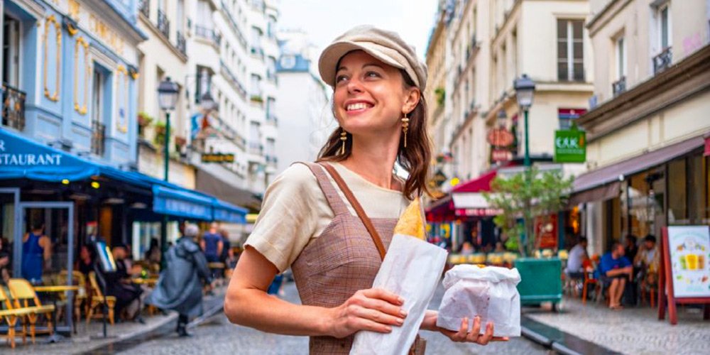 A young woman walks the streets of the Marais carrying a baguette and pastries