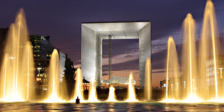 The Grande Arche at La Defense, flanked by lighted fountains, against the night sky