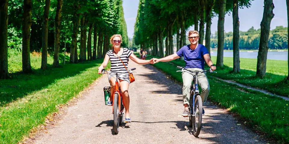 A couple holding hands while cycling on a path though the gardens of Versailles on a Bike Tour with Skip-the-Line Entrance
