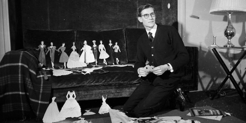 Yves Saint-Laurent cutting out miniature dress patterns in a black and white photo